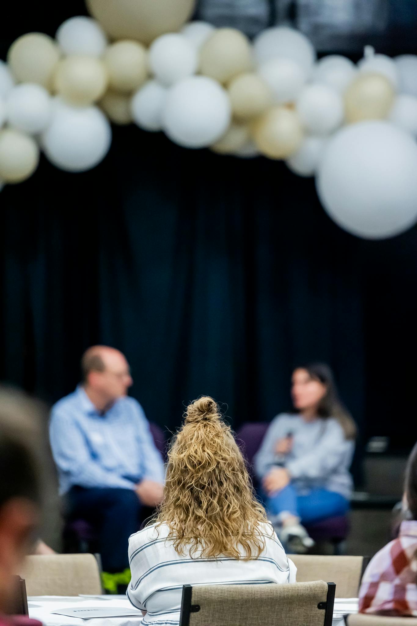 Attendees at a business seminar with speakers on stage and balloon decor theme.